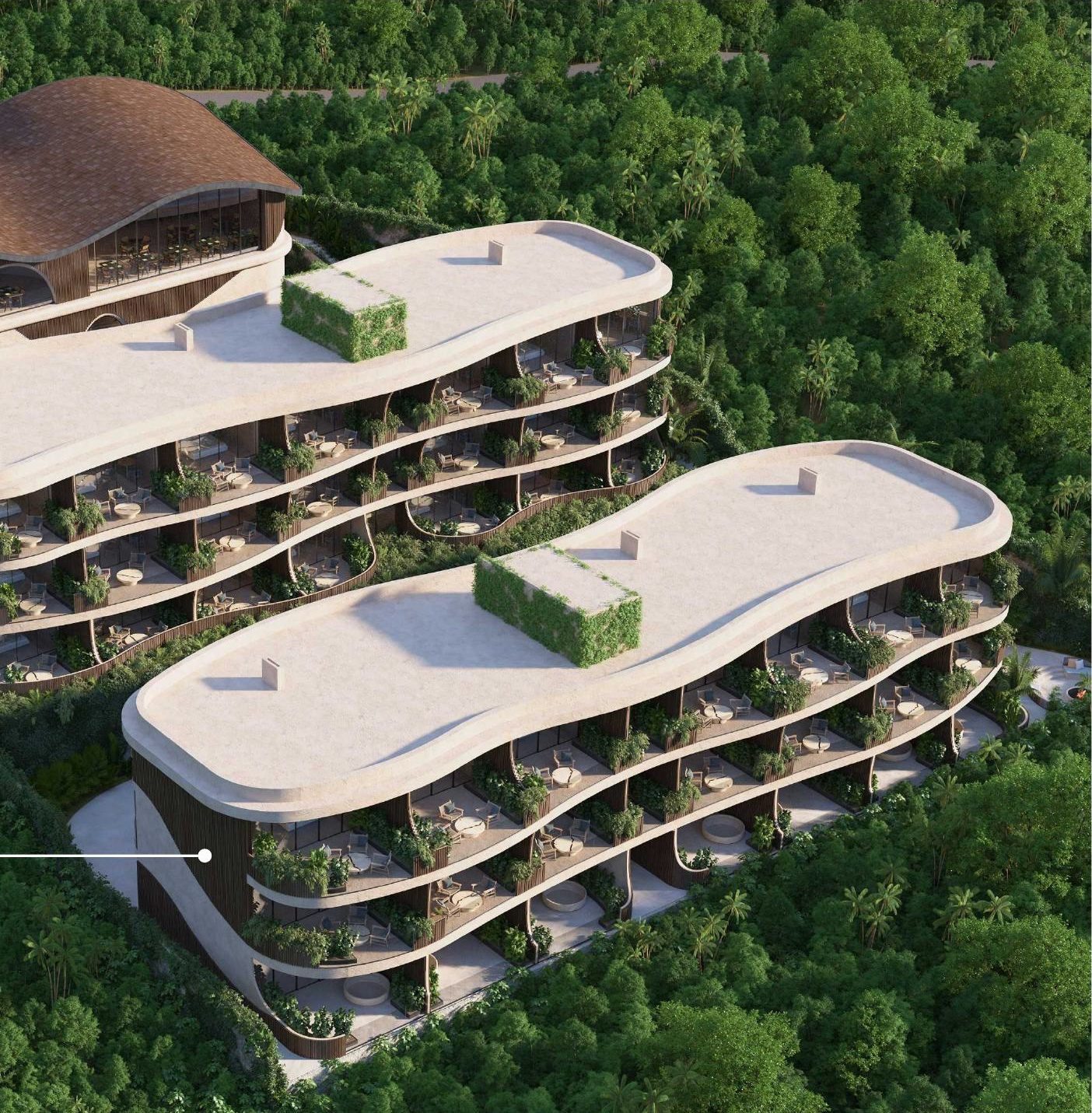 Aerial view of Luma's two residence buildings with wavy roofs set into dense Uluwatu jungle above the coastline