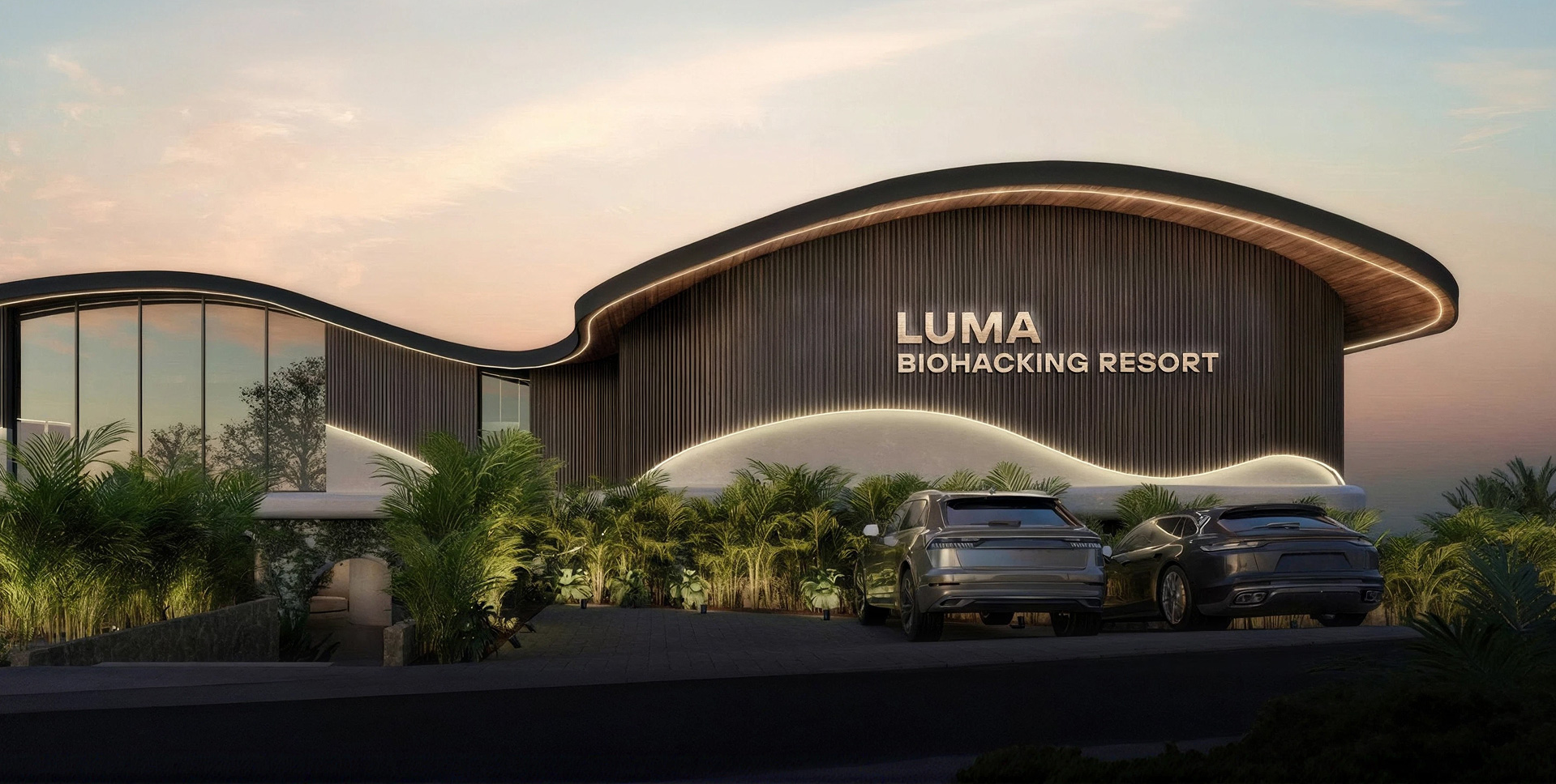 Luma Biohacking Resort at dusk — the wavy organic roofline lit against a warm sky, framed by tropical greenery on the cliffs of Uluwatu, Bali